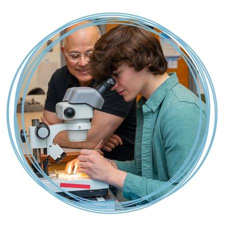 A faculty member assists a student with looking into a microscope